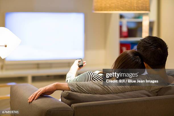 young couple watching tv on living room sofa - changing channels stock pictures, royalty-free photos & images