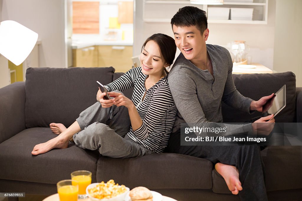 Young couple using smart phone on living room sofa