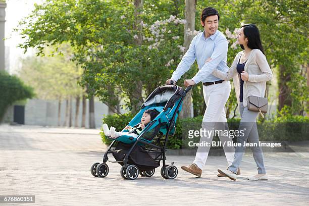 young couple taking a walk with their baby in pram - ベビーカー ストックフォトと画像