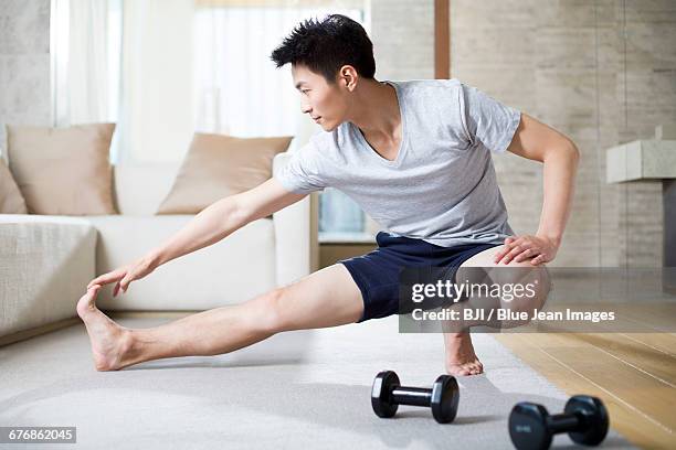 young man exercising at home - touch toes stock-fotos und bilder