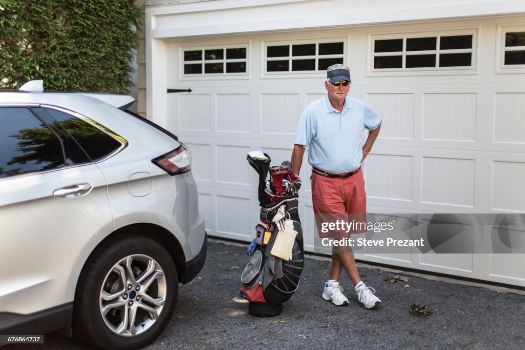 Portrait of senior male golfer standing next to garage door with golf bag