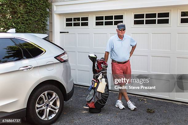 portrait of senior male golfer standing next to garage door with golf bag - old garage at home stock pictures, royalty-free photos & images