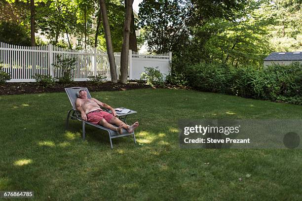 senior man sunbathing in garden listening to earphones - lounge chair stock pictures, royalty-free photos & images