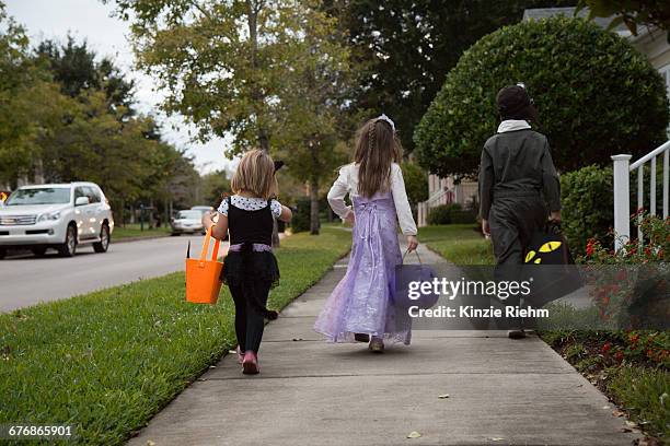 rear view of boy and sisters trick or treating walking on sidewalk - dreiviertel rückansicht stock-fotos und bilder