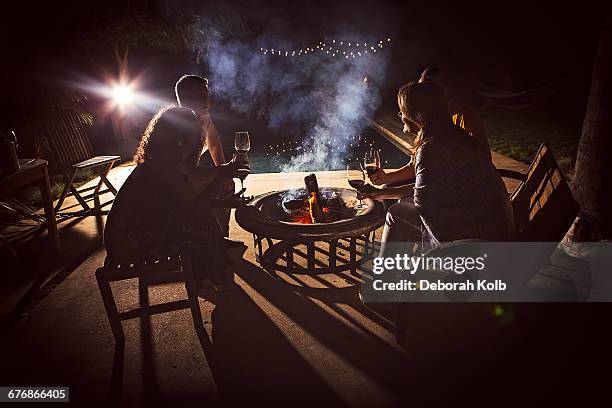 four mature adults sitting together around patio fire at night - hot latin nights stock pictures, royalty-free photos & images
