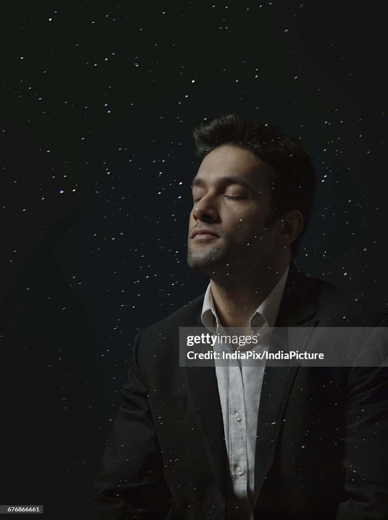 Man thinking with closed eyes in digitally composed glowing lights or starry sky