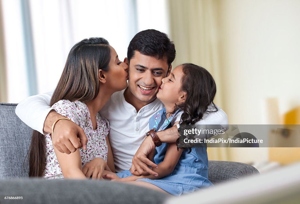 Happy family sitting on sofa mother and daughter kissing father