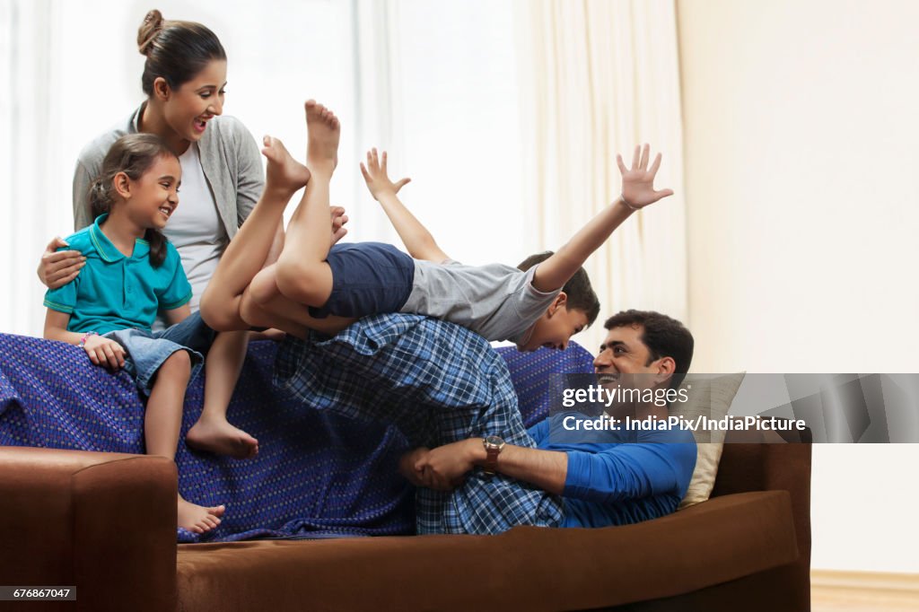 Playful father lifting son overhead on sofa