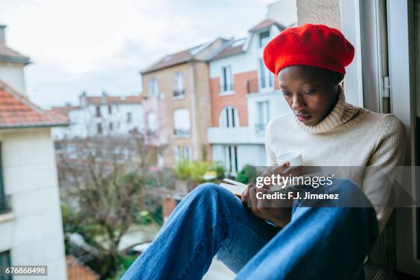 young woman sitting on window reading - black hat stock pictures, royalty-free photos & images