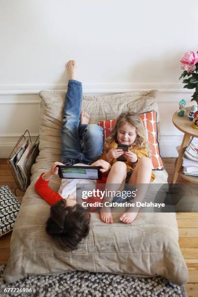 a brother and a sister looking at a tablet and a smartphone - tablette numérique stockfoto's en -beelden