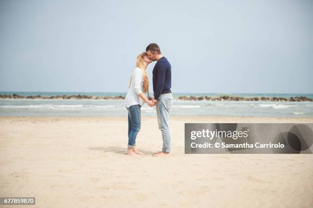 pregnant couple kissing on the beach. hand in hand. casual clothes. - ambientazione tranquilla stock-fotos und bilder