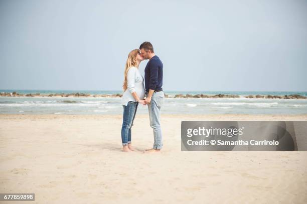 pregnant couple kissing on the beach. hand in hand. casual clothes. - coppia eterosessuale stock-fotos und bilder