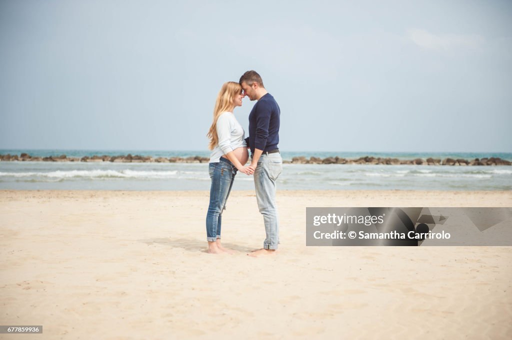 Pregnant couple on the beach. Hand in hand. Casual clothes.