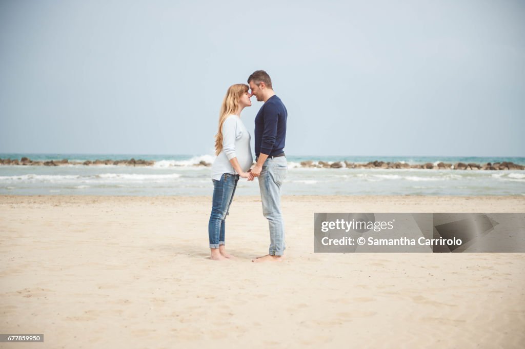 Pregnant couple on the beach. Hand in hand. Casual clothes.