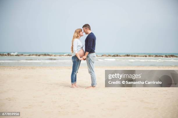 pregnant couple on the beach. hand in hand. casual clothes. - vivere semplicemente stockfoto's en -beelden
