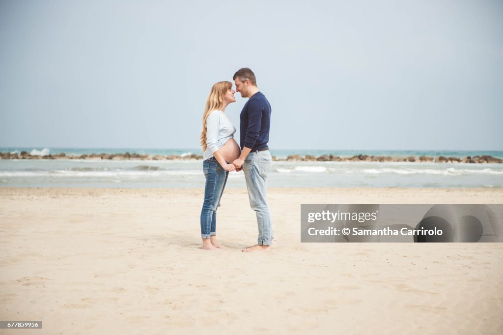 Pregnant couple on the beach. Hand in hand. Casual clothes.