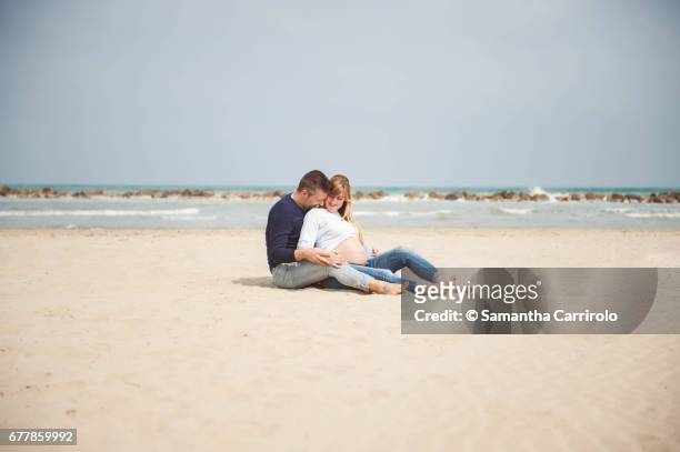 pregnant couple sitting on the beach. embrace. casual clothes. - darsi la mano stock pictures, royalty-free photos & images