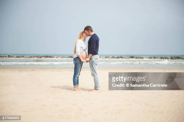 pregnant couple kissing on the beach. hand in hand. casual clothes. - ambientazione tranquilla stockfoto's en -beelden