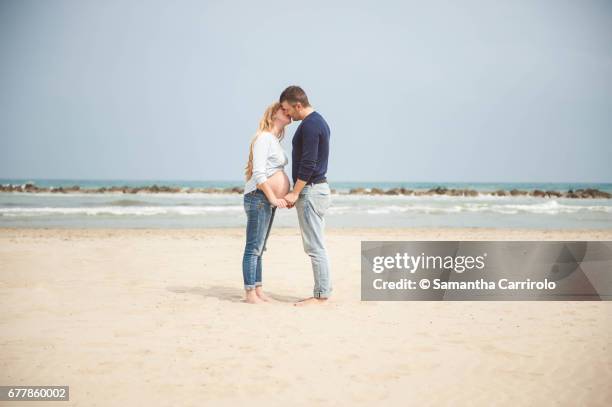 pregnant couple kissing on the beach. hand in hand. casual clothes. - serenità imagens e fotografias de stock