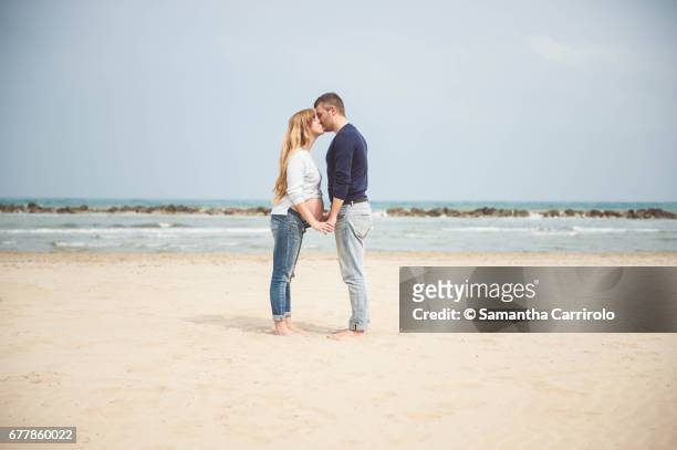 pregnant couple kissing on the beach. hand in hand. casual clothes. - serenità imagens e fotografias de stock