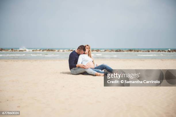 pregnant couple sitting on the beach. embrace. casual clothes. - darsi la mano stock pictures, royalty-free photos & images