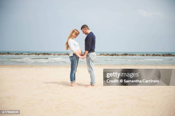 pregnant couple on the beach. hand in hand. looking at the belly. casual clothes. - evasione dalla realtà fotografías e imágenes de stock