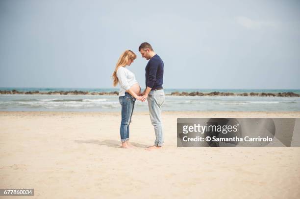 pregnant couple on the beach. hand in hand. looking at the belly. casual clothes. - darsi la mano stock pictures, royalty-free photos & images