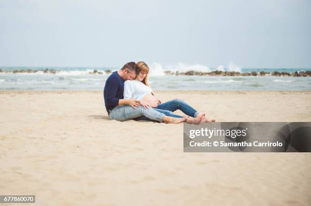 pregnant couple sitting on the beach. embrace. casual clothes. - ambientazione tranquilla stock-fotos und bilder