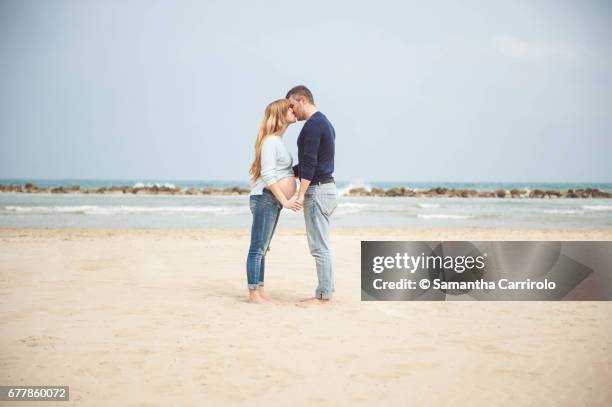 pregnant couple kissing on the beach. hand in hand. casual clothes. - serenità imagens e fotografias de stock