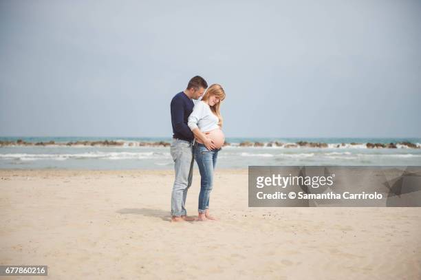 pregnant couple on the beach. hands on the belly. embrace. casual clothes. - coppia eterosessuale stock-fotos und bilder