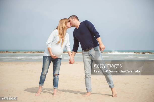 pregnant couple kissing on the beach. hand in hand. casual clothes. hand on the belly. - darsi la mano stock pictures, royalty-free photos & images