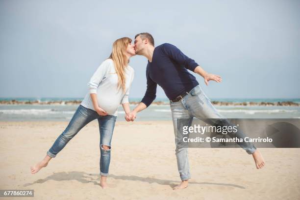 pregnant couple kissing on the beach. hand in hand. casual clothes. hand on the belly. - vivere semplicemente stockfoto's en -beelden