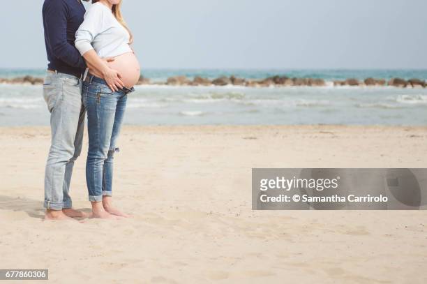 pregnant couple on the beach. hands on the belly. embrace. casual clothes. - relazione di coppia stockfoto's en -beelden