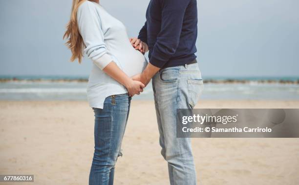 pregnant couple on the beach. hands on the belly. casual clothes. hand in hand. - sabbia stockfoto's en -beelden