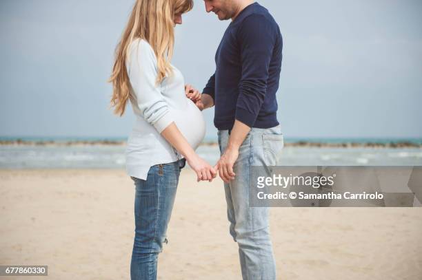 pregnant couple on the beach. hands on the belly. casual clothes. hand in hand. - coppia eterosessuale stock-fotos und bilder