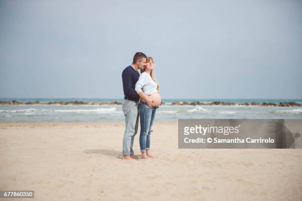 pregnant couple on the beach. hands on the belly. embrace. casual clothes. - coppia eterosessuale stock-fotos und bilder