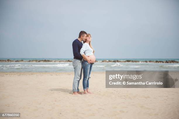 pregnant couple on the beach. hands on the belly. embrace. casual clothes. - relazione di coppia stockfoto's en -beelden