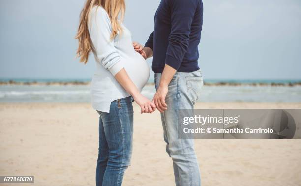 pregnant couple on the beach. hands on the belly. casual clothes. hand in hand. - serenità stockfoto's en -beelden