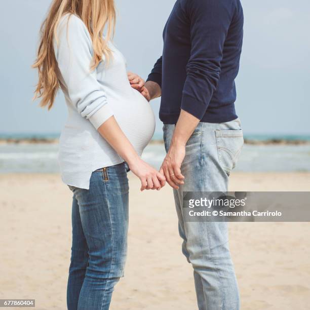 pregnant couple on the beach. hands on the belly. casual clothes. hand in hand. - sabbia stockfoto's en -beelden