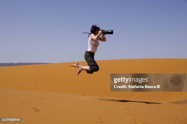 young woman jumps high in the desert holding a camera in her hands - donne di età media stock-fotos und bilder