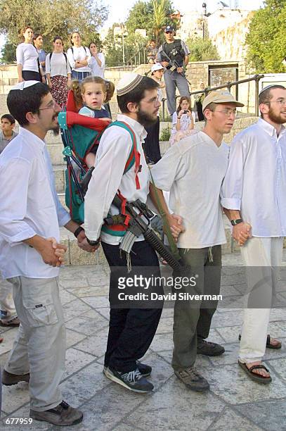 Religious Jew carries his child on his back and his machine gun on his side May 21, 2001 as he dances beside the walls of Jerusalem's Old City during...