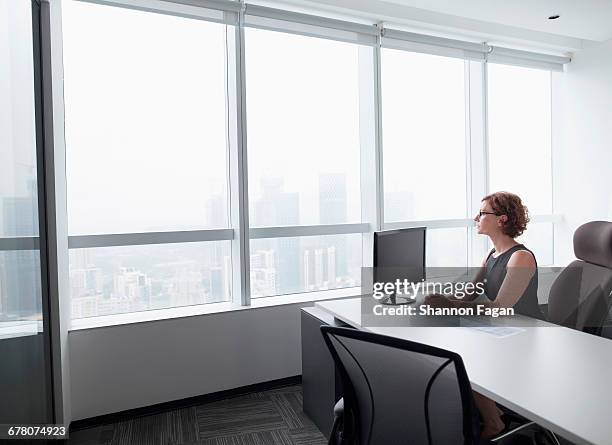 businesswoman in office looking out of window - office desk top view stockfoto's en -beelden