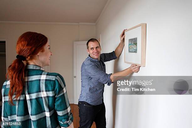 man holding frame on wall, woman looking on - blank frame stockfoto's en -beelden