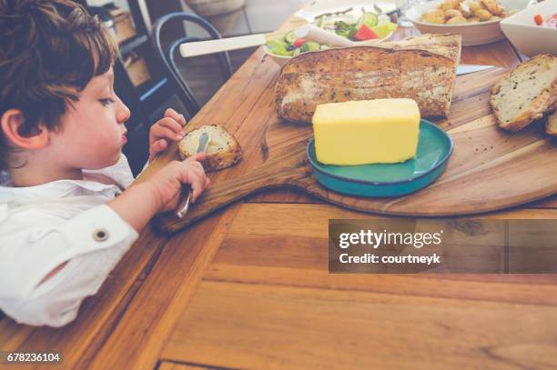 muchacho joven poniendo mantequilla en su pan. - untar de mantequilla fotografías e imágenes de stock