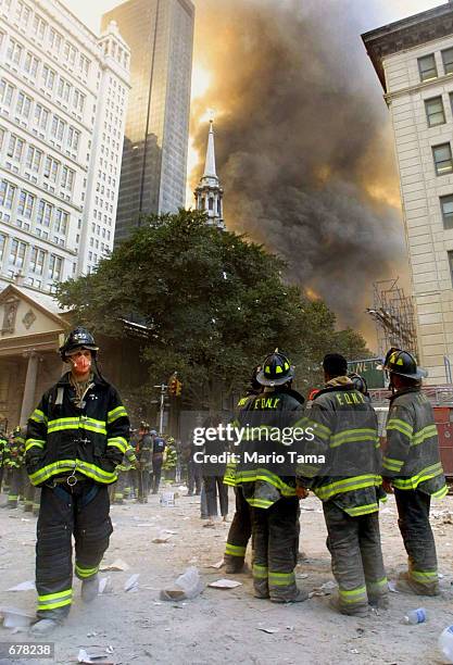 Firefighters watch as smoke rises from the site of the World Trade Center collapse September 11, 2001 in New York City after two hijacked airplanes...