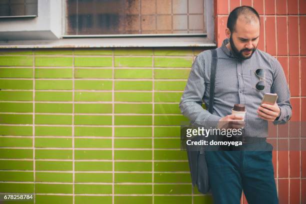 ung affärsman dricka kaffe och använder telefonen i staden gatan - carry on bag bildbanksfoton och bilder