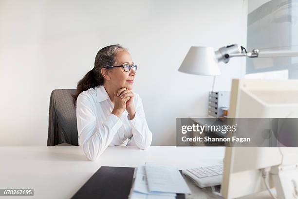 senior woman sitting at desk looking out of window - mature woman screen stock pictures, royalty-free photos & images