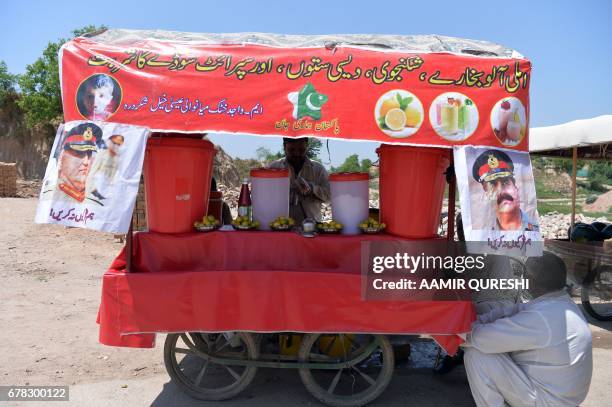 Pakistani vendor prepares lemon drinks for customers at his roadside stall, on which hang posters with images of Pakistan's army chief General Qamar...