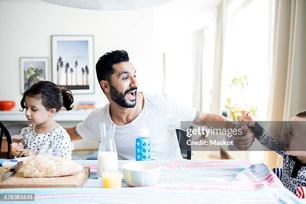 father playing with toddler while sitting by daughter during breakfast at home - milk family stock pictures, royalty-free photos & images