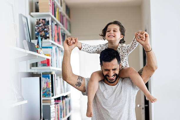 happy father carrying girl on shoulder while standing at home - happy kids stock pictures, royalty-free photos & images
